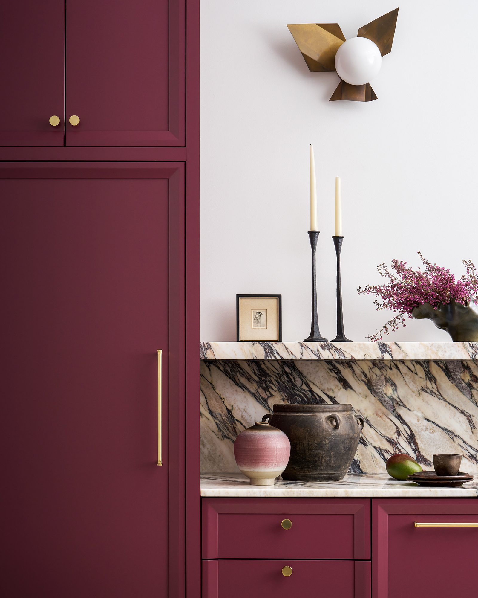 Modern kitchen with maroon cabinetry, marble countertops, and sleek lighting fixtures. Interior design photography retouching optimizes the color vibrancy, balances highlights and shadows, and removes distracting elements.