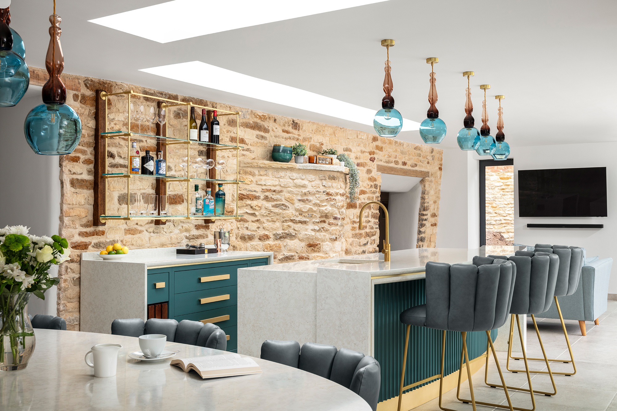 Open concept kitchen design featuring an island with bar seating, and a stone wall with a wine rack.