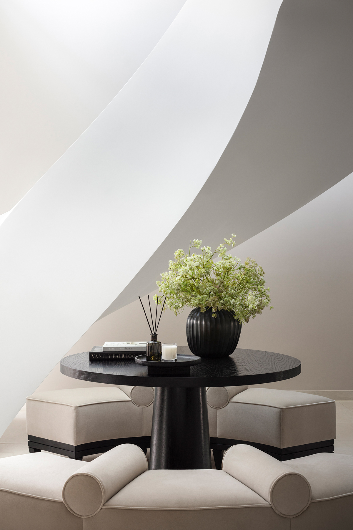 Round dark wood small table with a black vase and beige chairs.